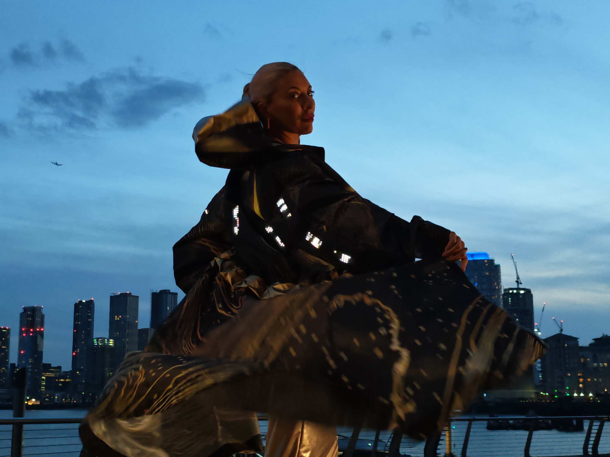 The illuminated black and gold CuteCircuit parka in motion against the evening skyline