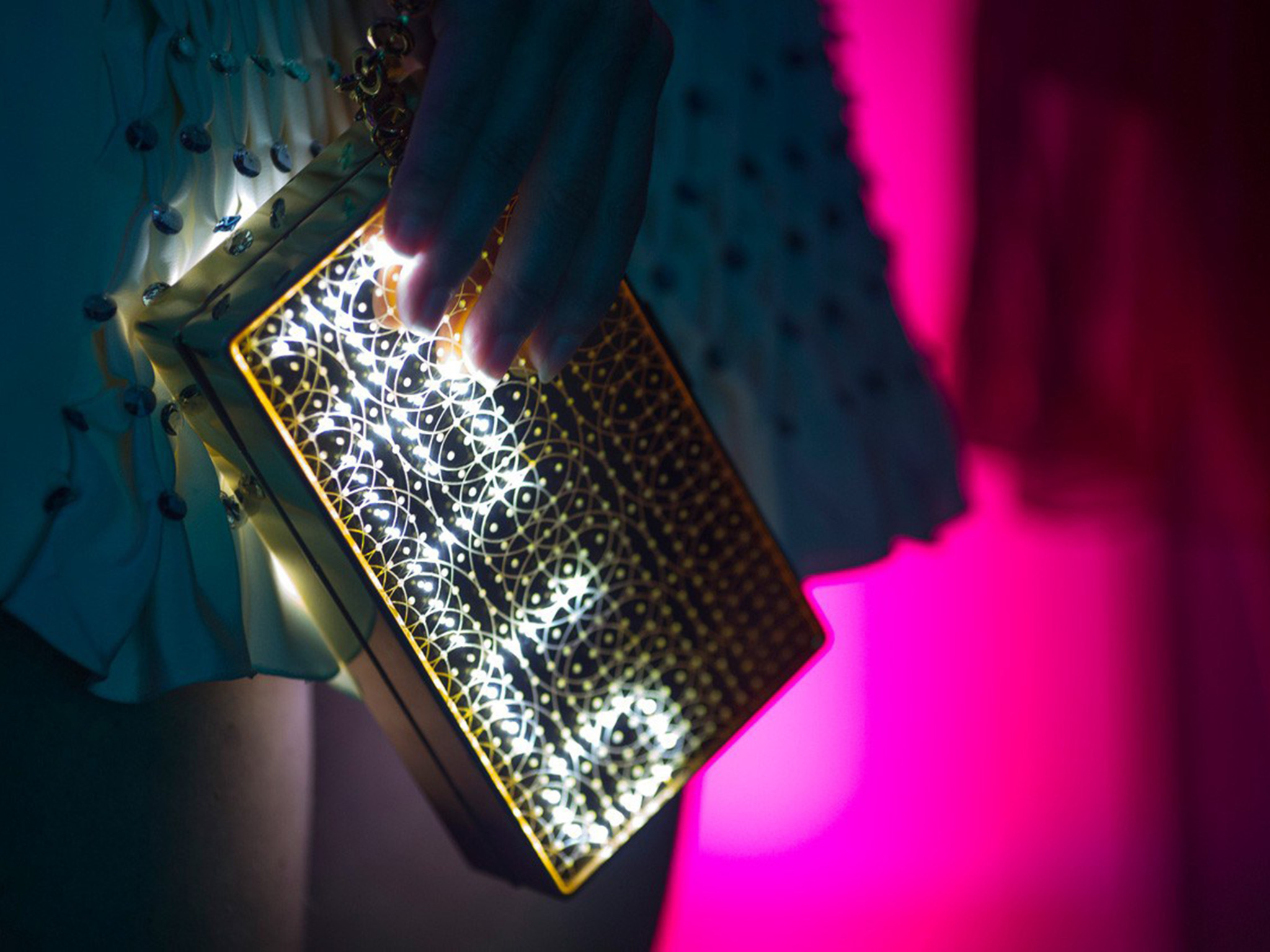 Close-up of the gold Mirror Handbag with illuminated geometric patterns against pink and blue light