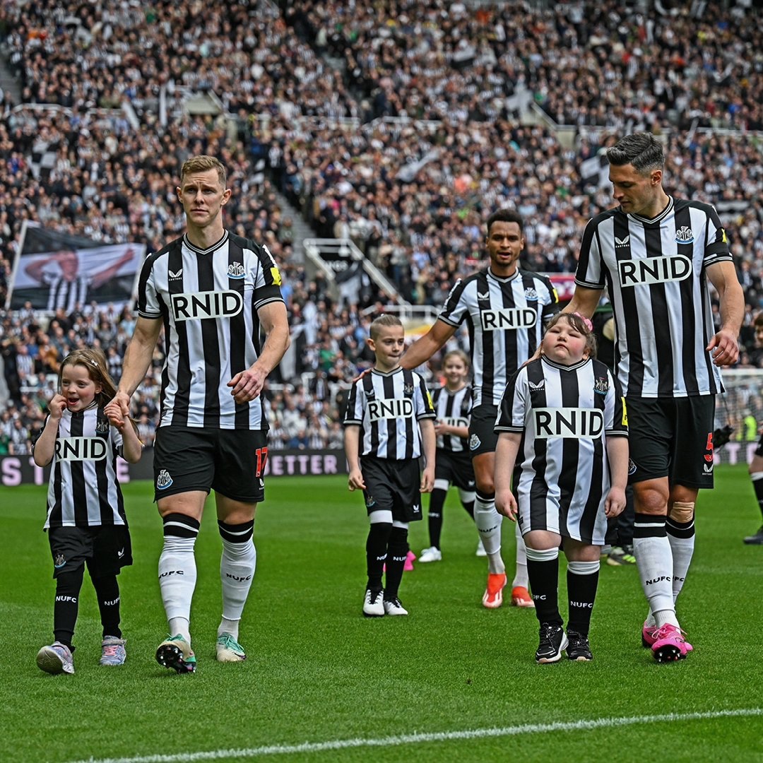 Newcastle United players and young mascots walking onto the pitch in front of packed stands at St James’ Park